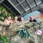 Three camp counselors and Frontier Horizon board member Jon Cline lean over a rock ledge at an indoor waterpark with tropical decor.