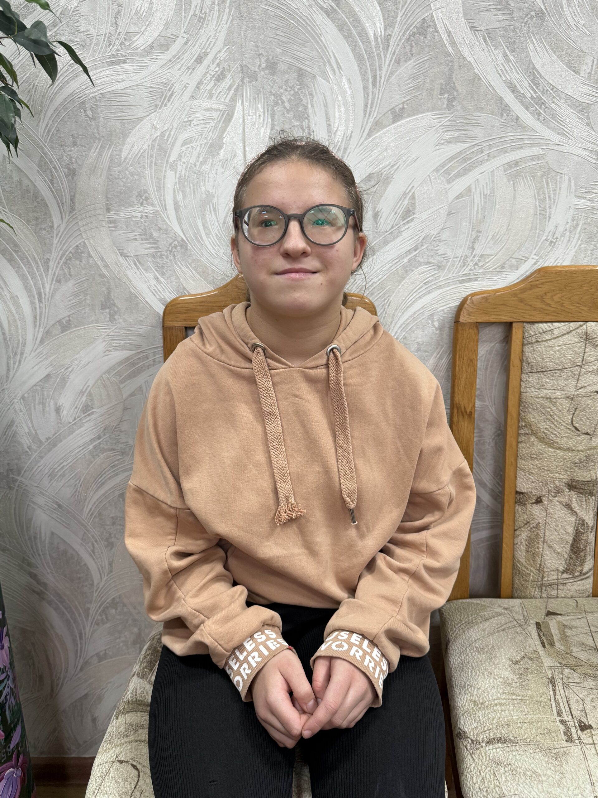 A cheerful 15-year-old Ukrainian girl named Evgeniia, smiling warmly at the camera. She has a friendly, upbeat expression and is photographed against a simple background.