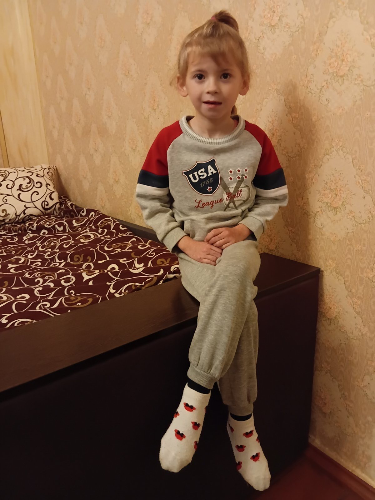 A sweet 4-year-old Ukrainian girl named Melania, looking gently at the camera with a soft, curious expression. She appears against a simple, neutral background.