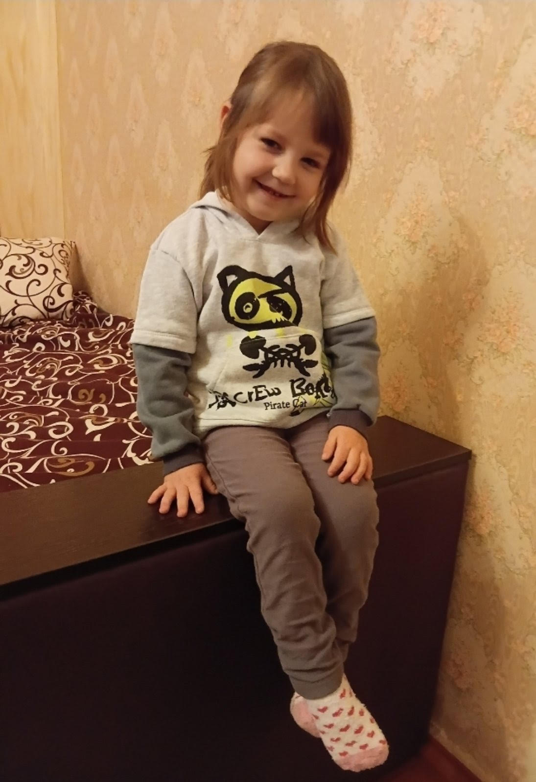A smiling 3-year-old Ukrainian girl named Milana, looking cheerful and bright. She has a sweet, playful expression and appears against a simple, neutral background.