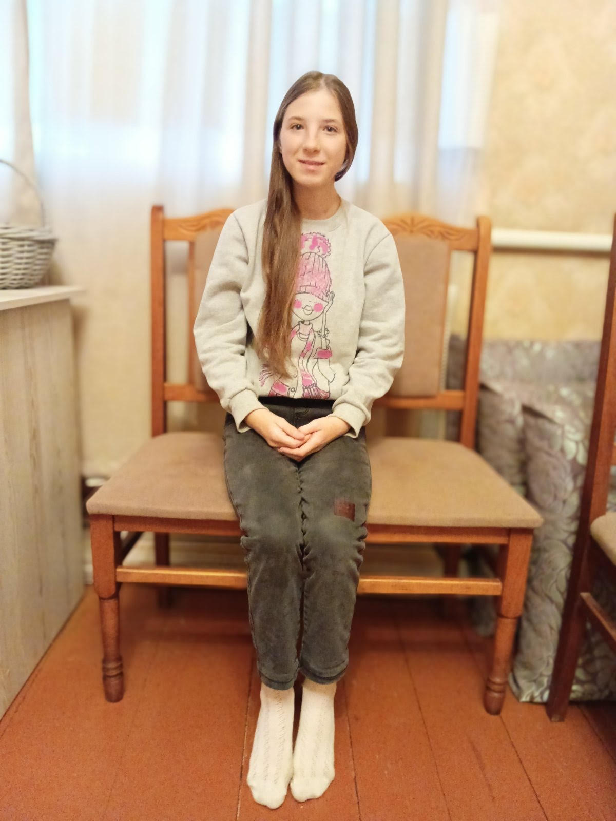 A smiling 14-year-old Ukrainian girl, Nadiya, looking softly at the camera. She has a calm, gentle expression and appears in simple, natural lighting against a neutral background.