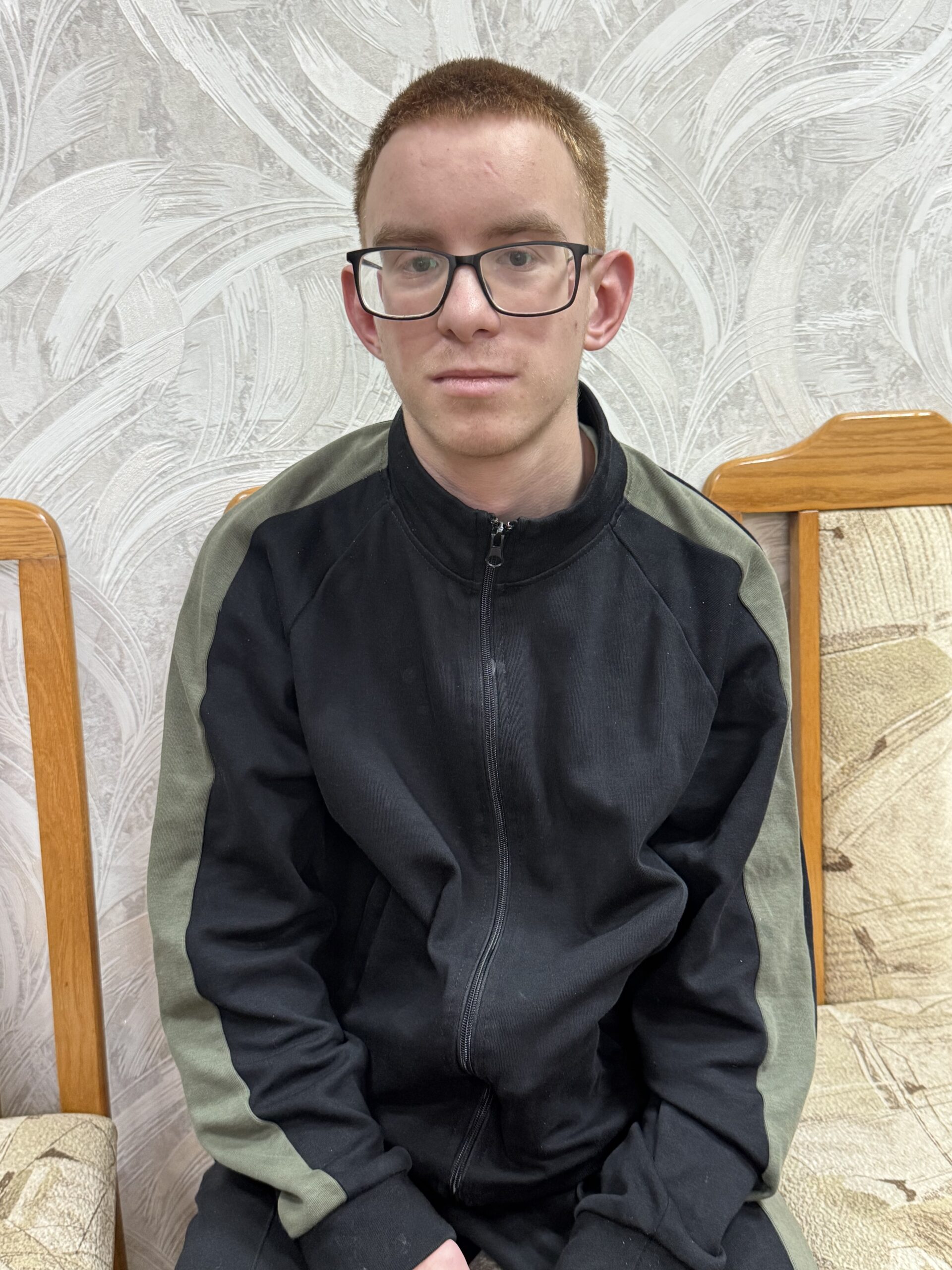 A friendly 15-year-old Ukrainian boy named Oleksandr, looking warmly at the camera with a gentle smile. He appears against a simple, neutral background.
